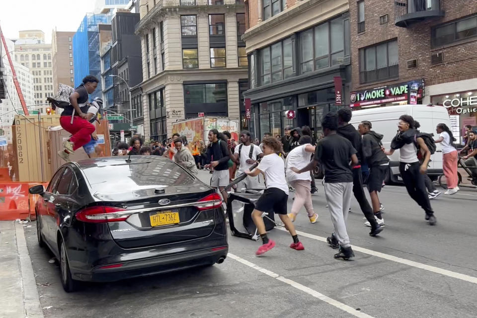 En este fotograma, un individuo salta sobre un auto mientras un grupo de personas corre por la calle en Broadway, cerca de Union Square, el viernes 4 de agosto de 2023. (AP Foto/Bobby Calvan)