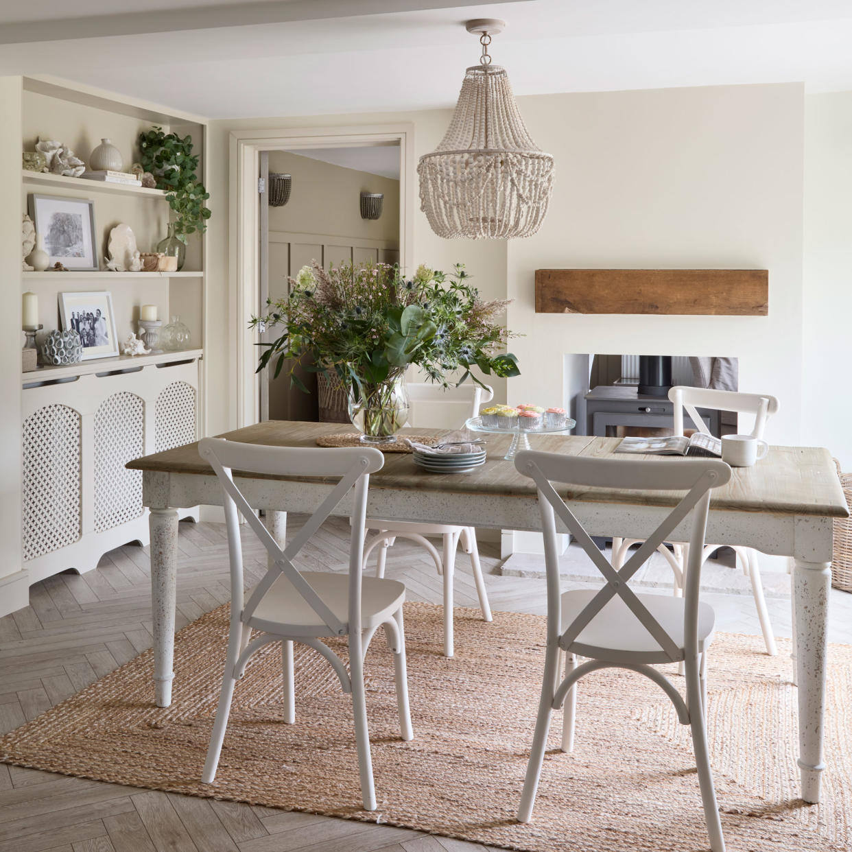  Dining area in a barn conversion with white wooden table and chairs and a beaded chandelier. 