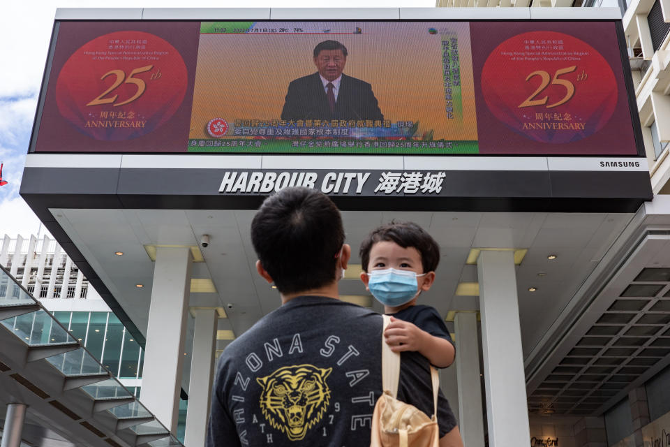 A man holding a child walks in front of a screen showing a live broadcast of Chinese President Xi Jinping speaking during a swearing-in ceremony for Hong Kong’s new chief executive John Lee, on July 1, 2022, in Hong Kong. - Credit: Getty Images