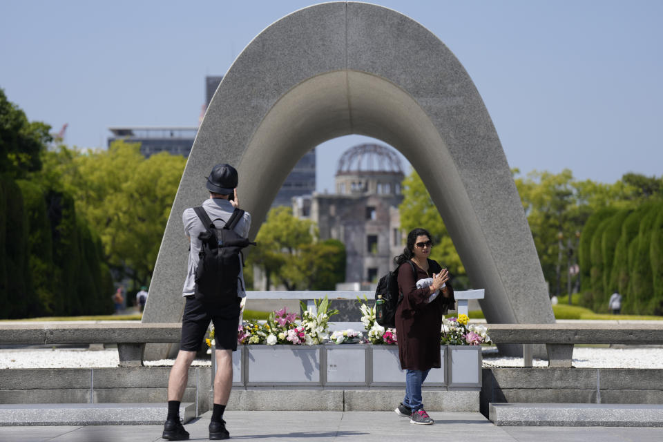 A visitor takes a photo as another finishes praying before flowers placed at the Hiroshima Peace Memorial Park, ahead of the Group of Seven nations' meetings in Hiroshima, western Japan, Wednesday, May 17, 2023. The G-7 summit starts Friday. (AP Photo/Hiro Komae)