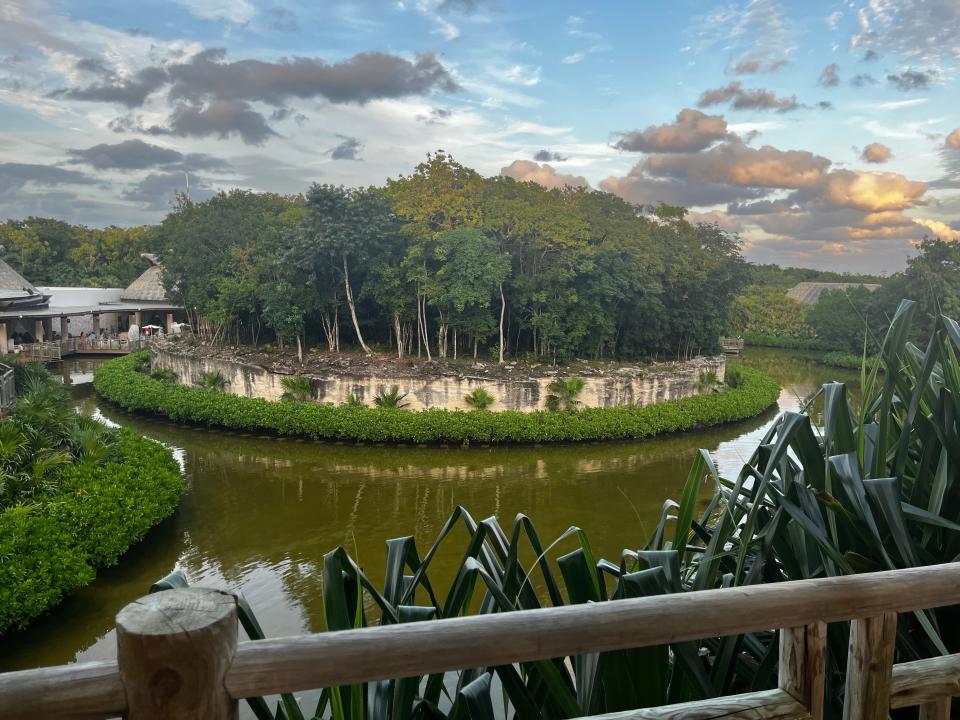 View from bridge of an island with lush greenery and trees. Grass is in the foreground and blue skies and clouds are overhead