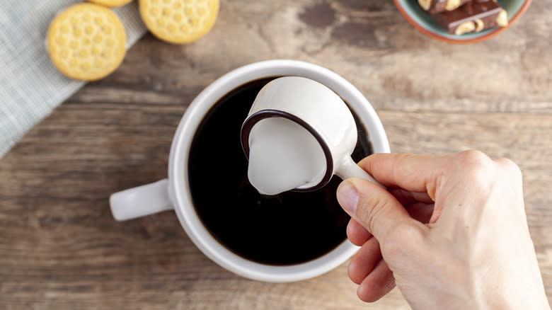 hand pouring cream into coffee