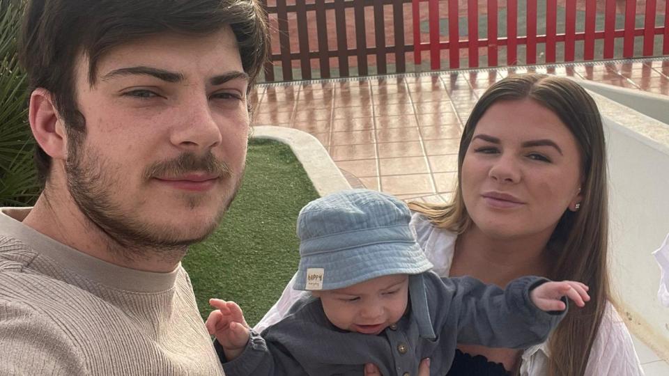 A young man and woman take a selfie with a baby
