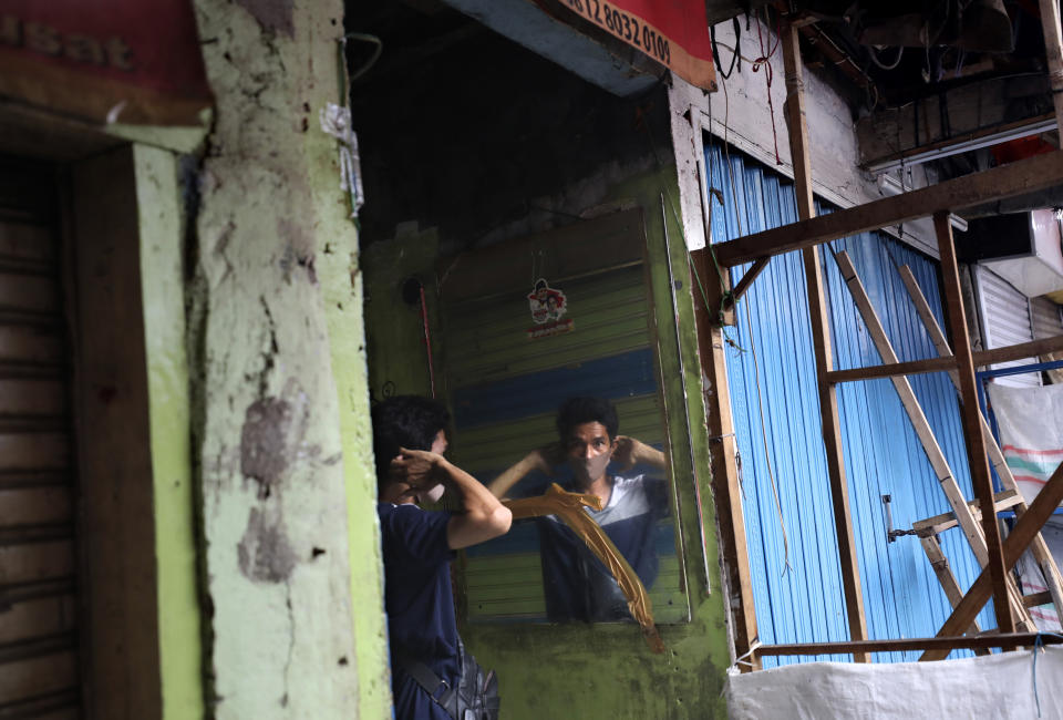 A man uses a mirror to put on a face mask at a market closed due to the coronavirus outbreak in Jakarta, Indonesia, Friday, April 10, 2020. Mosques usually filled for Friday prayers and streets normally clogged with cars and motorcycles were empty as authorities in Indonesia's capital enforced stricter measures to halt the coronavirus' spread after deaths spiked in the past week. (AP Photo/Dita Alangkara)