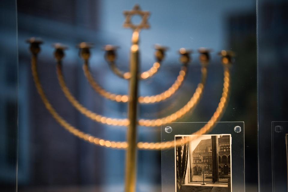 A photo showing the Hanukkah menorah belonging to the Posner family from Kiel, with a large swastika flag hanging from the facade of a building opposite, is part of an exhibition with items from Israel's Yad Vashem Holocaust memorial in the German parliament Bundestag in Berlin, Germany, Monday, Jan. 23, 2023. An exhibition marking the 70th anniversary of Israel's Yad Vashem Holocaust memorial brings back to Germany a diverse set of everyday objects that Jews took with them when they fled the Nazis.