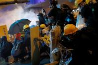 Demonstrators take cover under umbrellas as they face riot police during a protest against police violence in Hong Kong