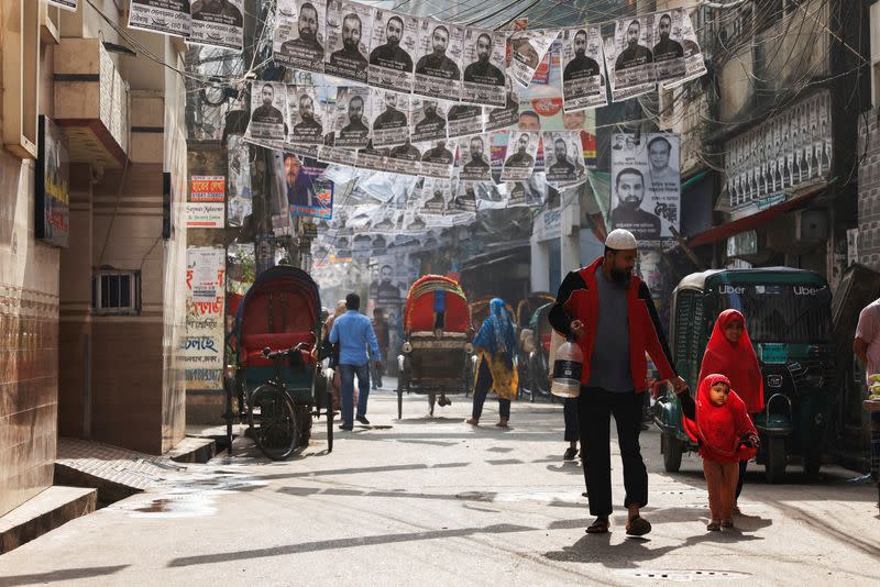 FILE PHOTO: Commuters pass by as posters of an election candidate hang on the street ahead of the general election in Dhaka