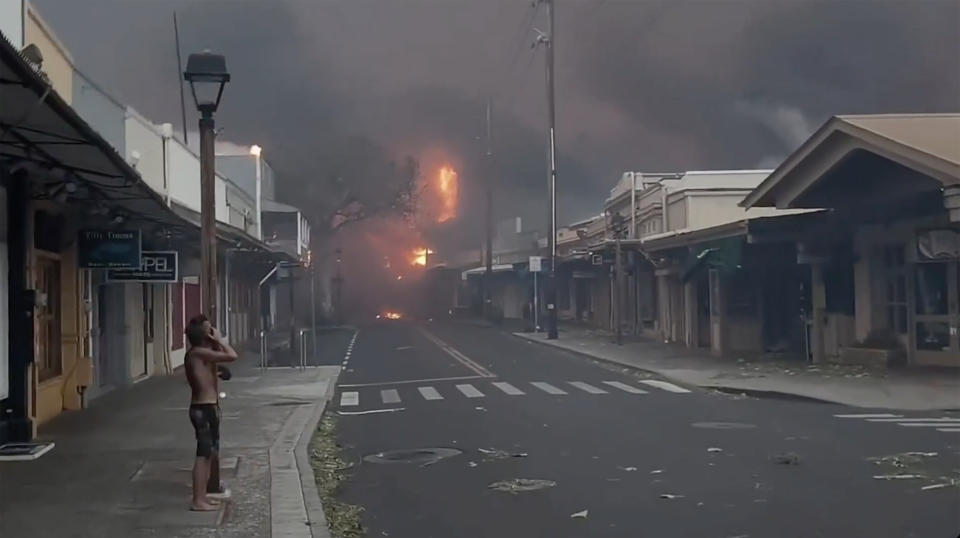 People watch as smoke and flames fill the air from raging wildfires on Front Street in downtown Lahaina, Maui on Tuesday, Aug. 8, 2023. Maui officials say wildfire in the historic town has burned parts of one of the most popular tourist areas in Hawaii. County of Maui spokesperson Mahina Martin said in a phone interview early Wednesday says fire was widespread in Lahaina, including Front Street, an area of the town popular with tourists. (Alan Dickar via AP