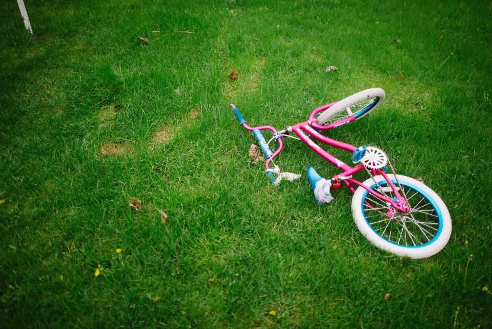 A pink child's bike rests on green grass.