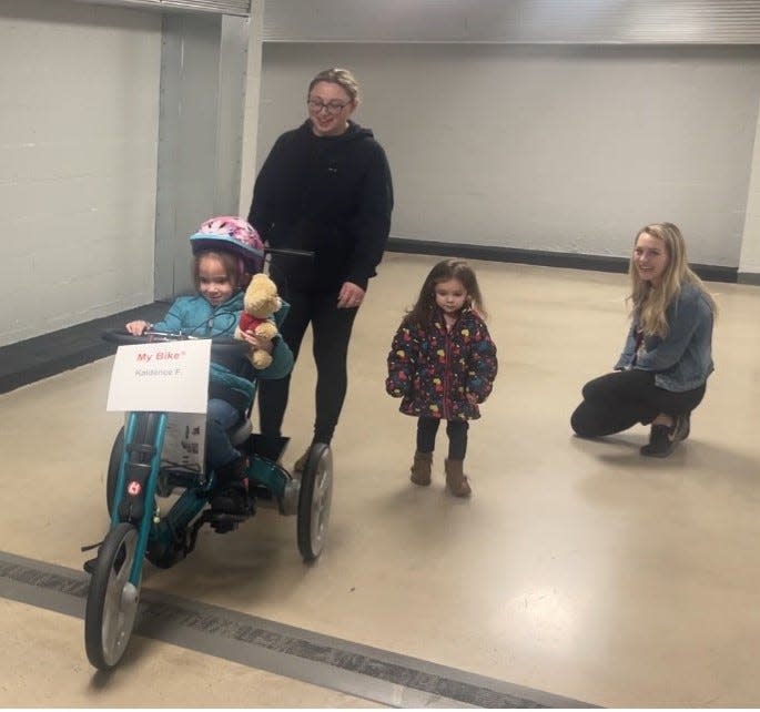 Kaidence gives a smile as she rides her new adaptive bike, with her mom Ashley, sister Macy and AIU8 physical therapist Kelsey Walker watching.