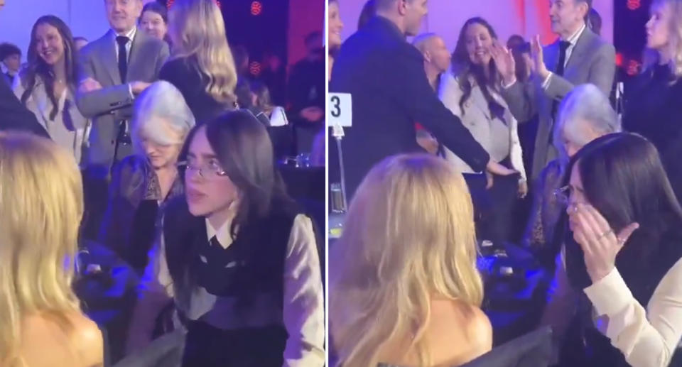 Billie Eilish speaks with Kylie Minogue in front of a crowd of people.