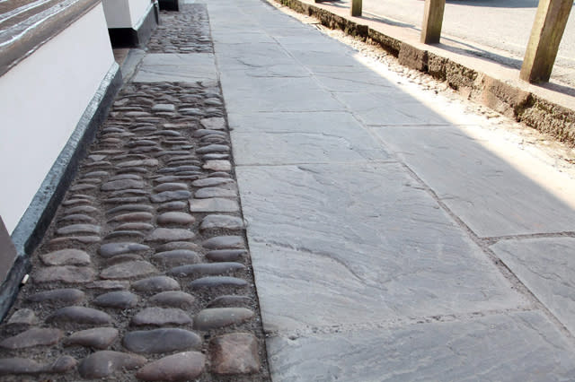 FILE PICTURE - The cobbled streets in Dunster, Somerset with a new path way made out of flag stones.  Paving slabs which replaced iconic cobbles in an historic medieval village are to be removed by a cash-strapped council at a cost of ï¿½45,000 - because they are "too blue".  See SWNS story SWPAVING.  The original stones which dated back to the Bronze Age was torn from a main road in Dunster, Somerset, to improve pedestrian safety and disabled access.  The stones were replaced with blue-hued slabs, which locals complained were too blue, angular, regular, smooth and "like a path on a new housing estate".  Villagers accused the council of 'vandalism' and Historic England was furious that it was not consulted before the work began.  Now, just ten months later, the council has agreed to change the paving slabs to stones which are more in-keeping with the village - at a cost to taxpayers of ï¿½45,000.  It comes after the cash-strapped Tory approved budget cuts of ï¿½16 million earlier this year. 