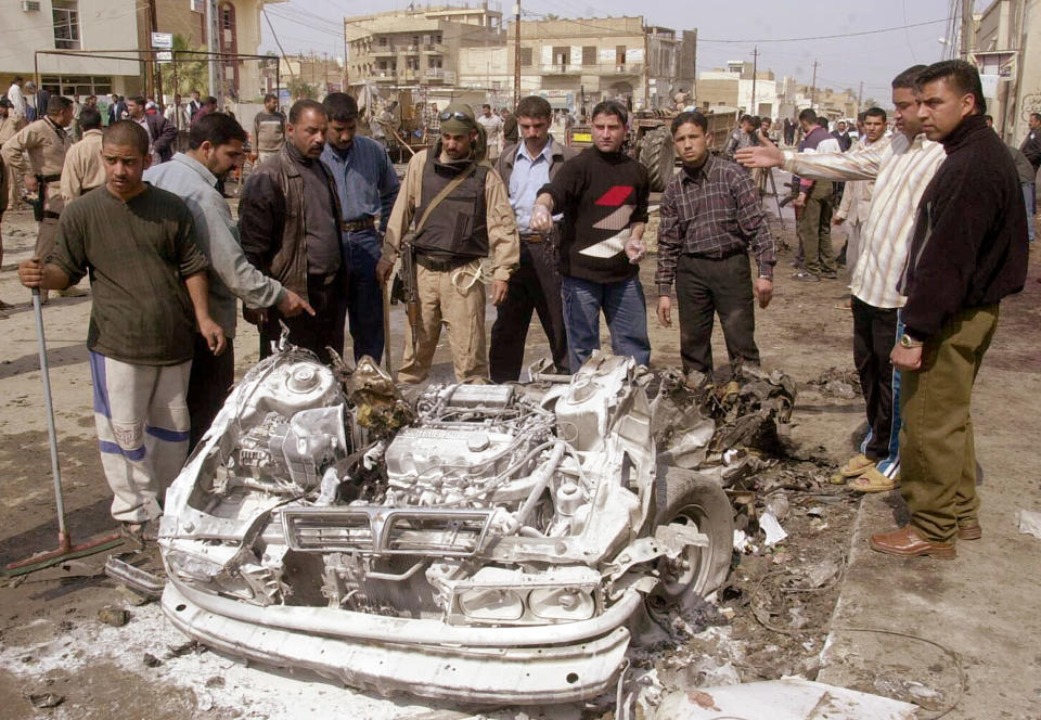 Iraqi residents of the town of Hilla stand around the debris of a massive car bomb which killed at least 125 people and injured over 100 more February 28, 2005. A suicide car bomber drove his car at a line police recruits waiting for eye tests next to a busy market in the single bloodiest episode since the fall of Saddam Hussein. REUTERS/Ali Abu Shish AW/THI