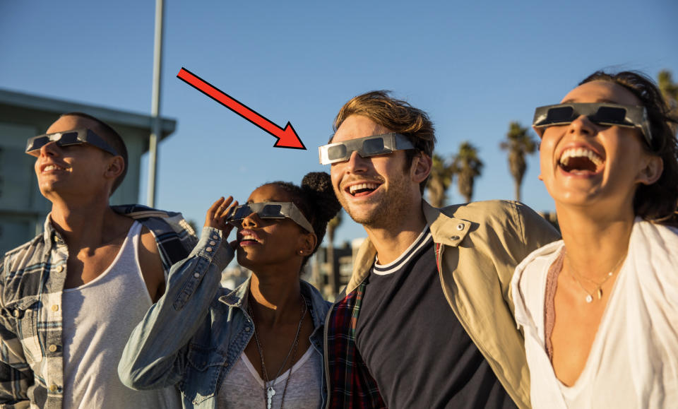 Four friends wearing eclipse glasses looking upwards with expressions of amazement