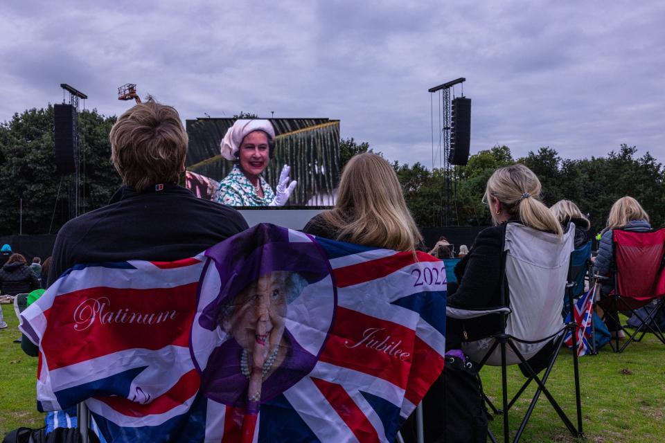 People sit in a chair decorated with a flag with the Queen's face on it in Hyde Park.