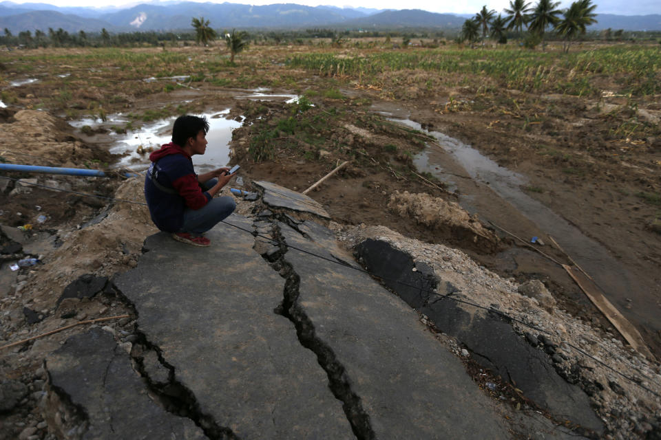 In this Saturday, Oct. 6, 2018, file photo, a man sits on a piece of asphalt from a road which was wiped out by earthquake-triggered liquefaction in Sigi, Central Sulawesi, Indonesia. (AP Photo/Dita Alangkara, File)