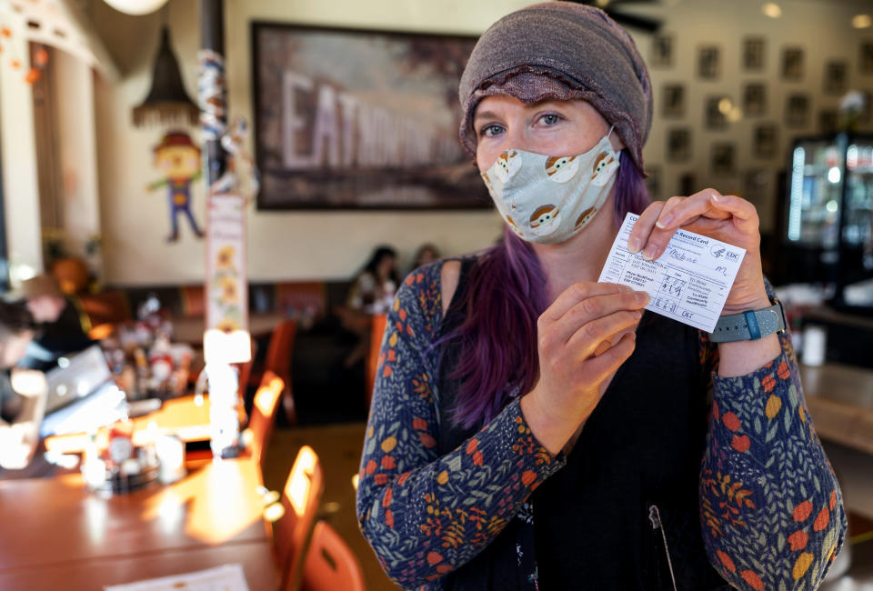 Melanie Bolen, a personal trainer, shows her vaccination card before being allowed to sit inside the Fred 62 restaurant in the Los Feliz neighborhood of Los Angeles, Monday, Nov. 29, 2021. Enforcement began Monday in Los Angeles for one of the strictest vaccine mandates in the country, a sweeping measure that requires proof of COVID-19 shots for everyone entering a wide variety of businesses from restaurants to theaters and gyms to nail and hair salons. (AP Photo/Damian Dovarganes)