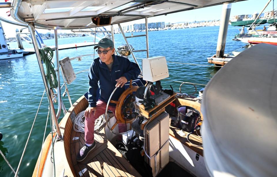 A man holds the steering wheel on a knot anchored in a harbor.