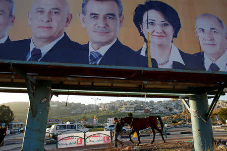 FILE PHOTO: A man walks with a horse near a campaign poster for the National Democratic Assembly party in the Israeli-Arab city of Umm el-Fahm January 14, 2013. REUTERS/Ammar Awad/File Photo