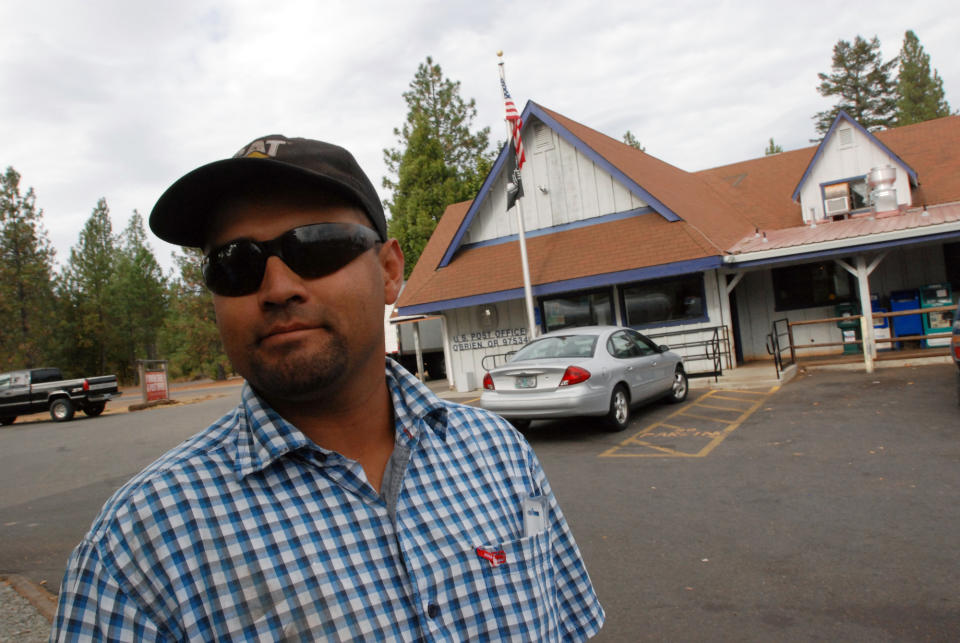 In this Oct. 12, 2012, photo, Hector Guzman poses for a photo in front of the post office in O'Brien, Ore., where cuts to sheriff's patrols prompted by the failure of a tax levy have inspired some local residents to organize armed patrols of the rural area of about 750 residents. Guzman, whose home was burglarized several years ago, said he likes the idea of people watching out for each other. (AP Photo/Jeff Barnard)