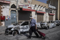 A man passes by cars torched after a night of violence between Israeli Arab protesters and Israeli police in the mixed Arab-Jewish town of Lod, central Israel, Tuesday, May 11, 2021. (AP Photo/Heidi Levine)