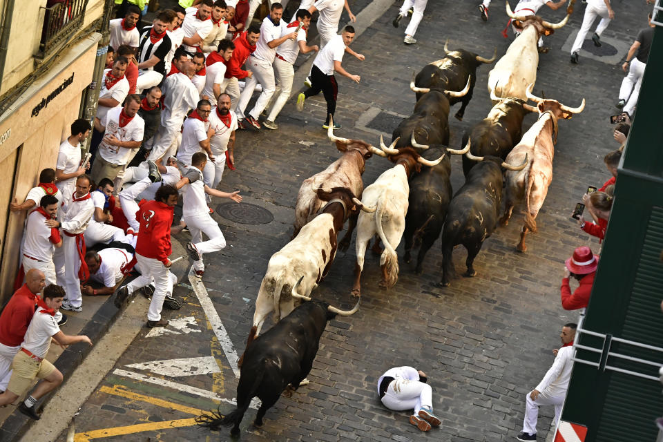 A runner falls as people run through the street with fighting bulls at the San Fermin Festival in Pamplona, northern Spain, Friday, July 8, 2022. Revellers from around the world flock to the city every year for nine days of uninterrupted partying in Pamplona's famed running of the bulls festival which was suspended for the past two years because of the coronavirus pandemic. (AP Photo/Alvaro Barrientos)