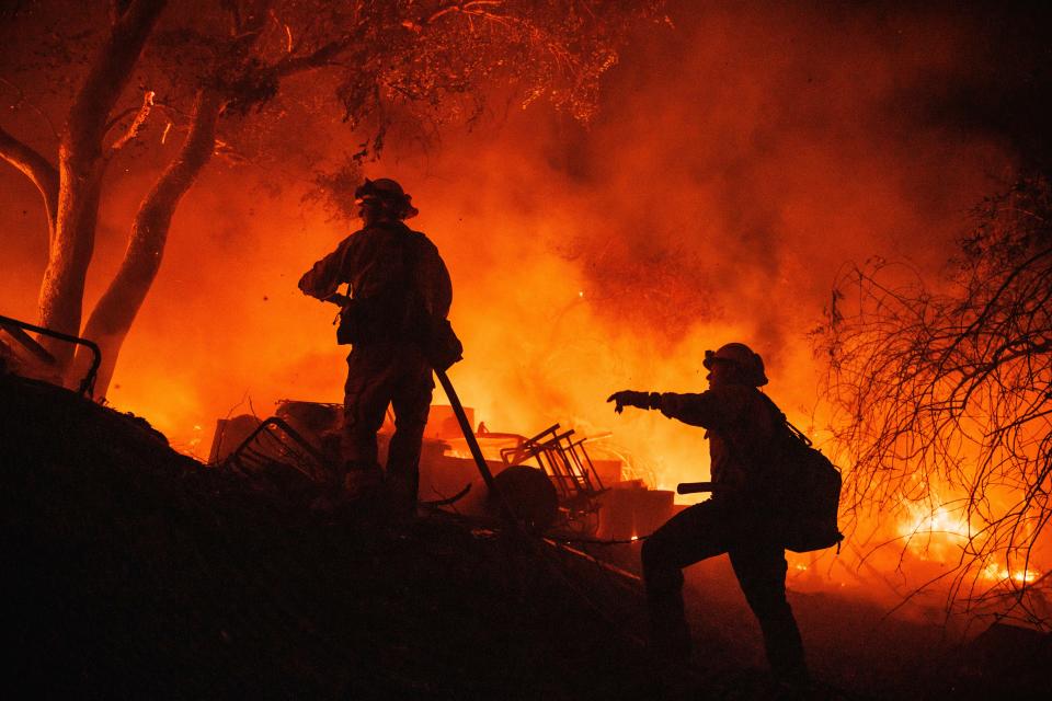 Firefighters coordinate efforts at a burning property while battling the Fairview Fire on Monday near Hemet, Calif.