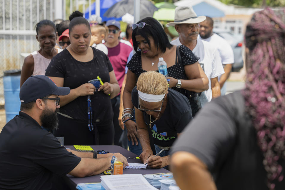 Personas formadas para ser atendidas por el Dr. Pedro Juan Vázquez, conocido por su nombre artístico PJ Sin Suela, en Loiza, Puerto Rico, el sábado 25 de mayo de 2024. El médico de 34 años viaja desde la capital de San Juan hasta el sur de la isla. y regiones centrales para atender a las comunidades que luchan tras los huracanes. Después de colgar su bata de médico, Vázquez dedica su tiempo a producir nueva música que hable de los problemas de la isla. (Foto AP/Alejandro Granadillo)