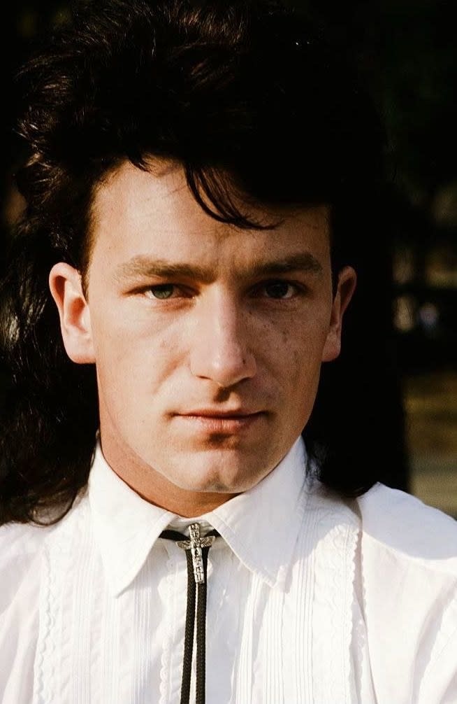 Bono posing for a portrait in a bolo tie with long, dark hair in 1983