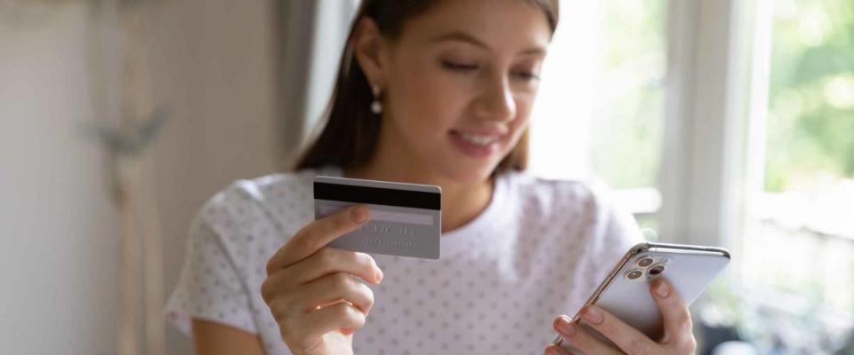 Happy young woman holding debit card and smartphone