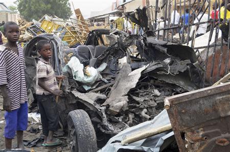 Two boys stand near the charred chassis of a vehicle after a bomb attack near a busy market area in Ajilari-Gomari near the city's airport, in Maiduguri March 2, 2014. REUTERS/Stringer