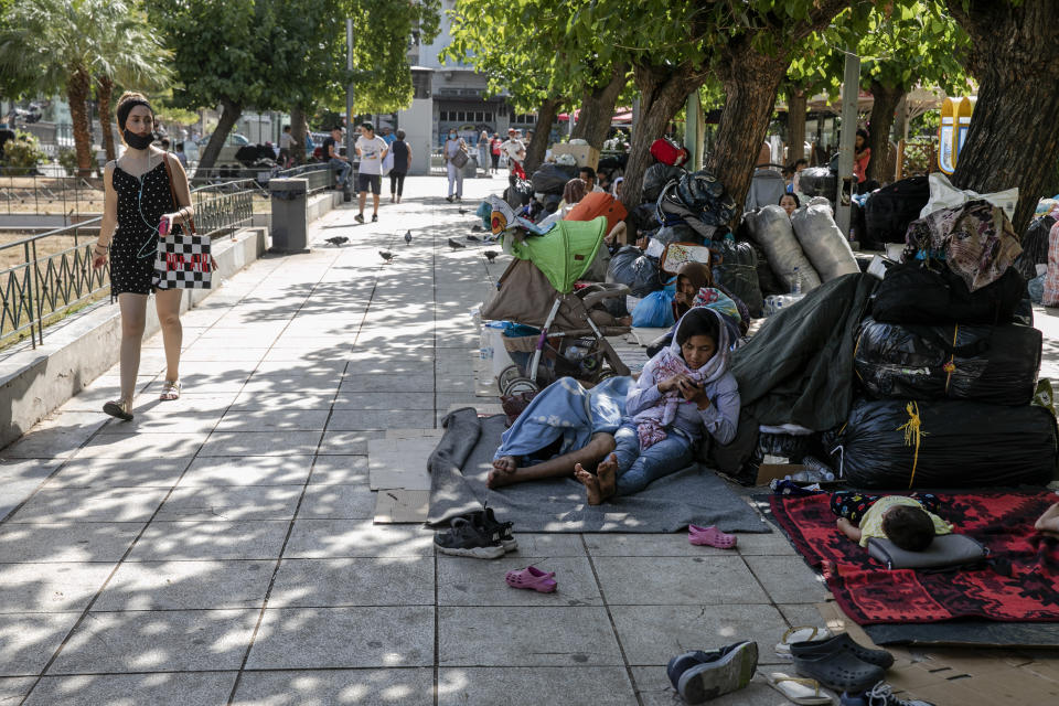 A woman looks at migrants who have camped at central Victoria square in Athens, on Wednesday, Sep. 2, 2020. Greece's Shipping Minister says Greek authorities have managed to prevent the arrival of thousands of migrants seeking to enter Greece clandestinely by sea despite a recent lack of cooperation from the Turkish coast guard. (AP Photo/Yorgos Karahalis)