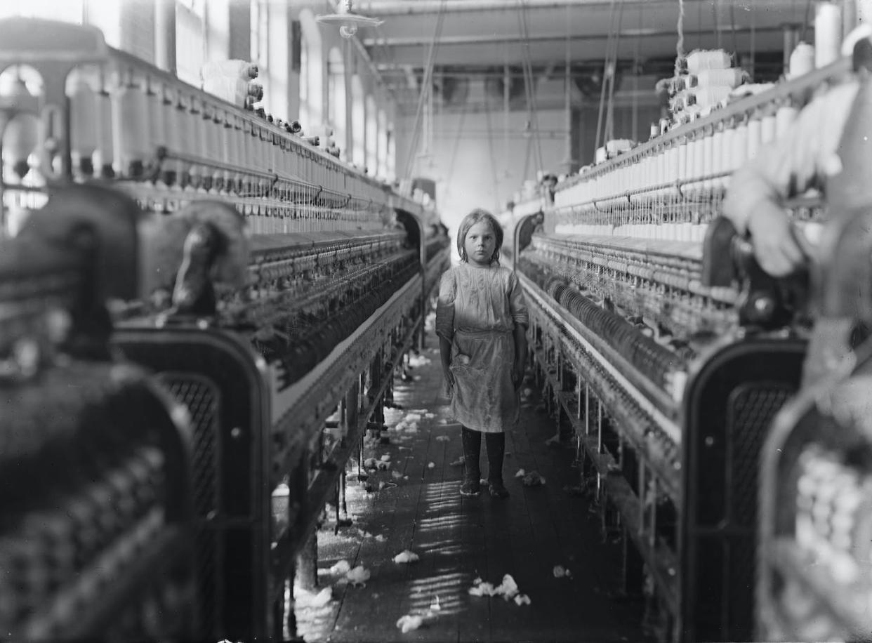 Fotografía de Lewis W. Hine de una pequeña hilandera en Mollohan Mills, Newberry, S.C: "Estaba atendiendo sus 'lados' de la maquinaria como una veterana, pero después de haber tomado la foto, el capataz se acercó y dijo en un tono de disculpa patético: 'Acaba de llegar'. Un momento después repitió la información. Parece que las fábricas están llenas de jóvenes que 'acababan' de llegar" o 'estaban ayudando a la hermana'".. <a href="https://commons.wikimedia.org/wiki/File:Child_laborer.jpg" rel="nofollow noopener" target="_blank" data-ylk="slk:National Child Labor Committee/Library of Congress;elm:context_link;itc:0;sec:content-canvas" class="link ">National Child Labor Committee/Library of Congress</a>