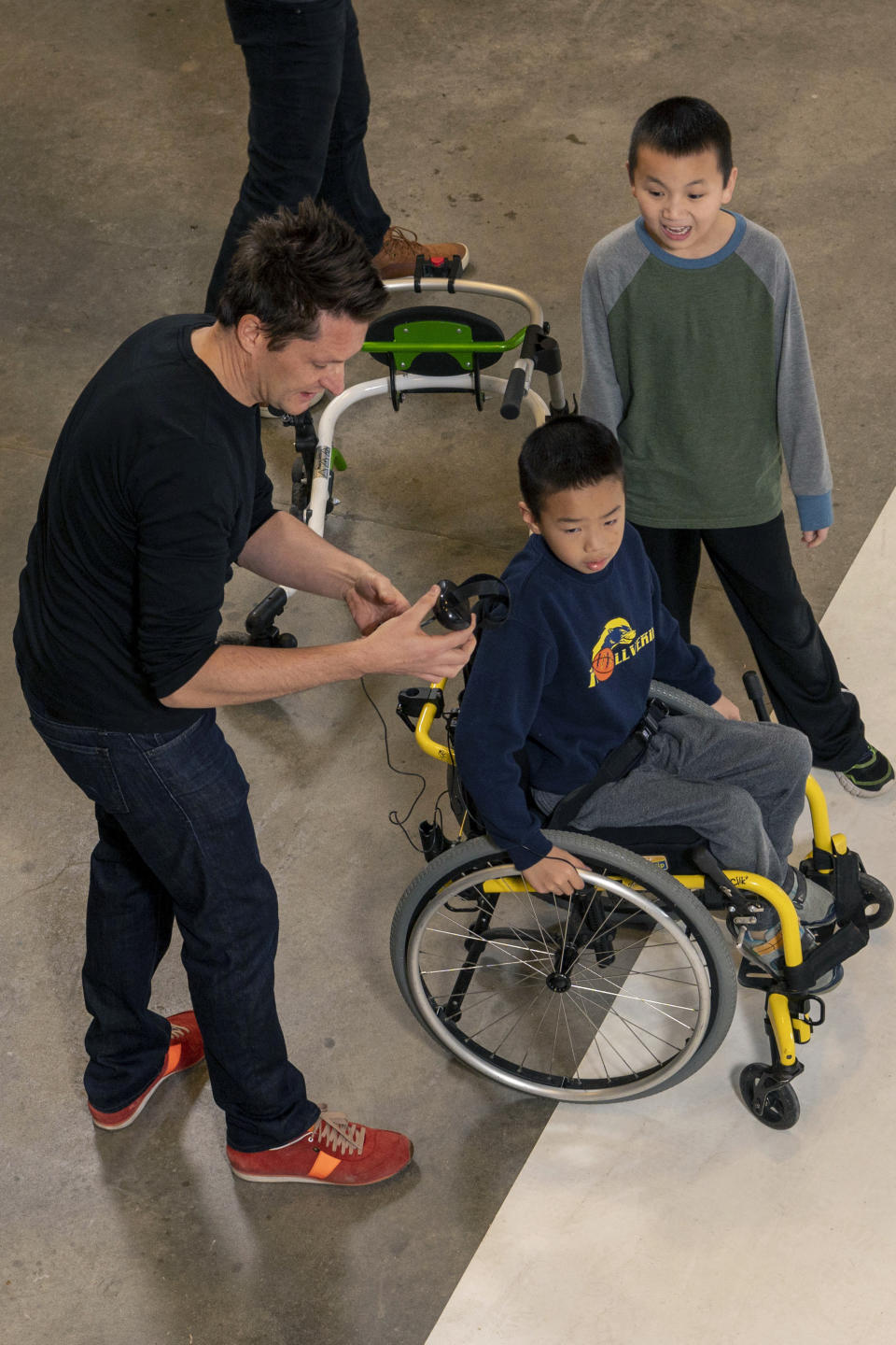 In this Nov. 17, 2019, photo provided by the University of Michigan, professor Roland Graf, left, readies the iGYM system before brothers Bryan Kreps, seated, and Darren Kreps play a game modeled after soccer and air hockey that is projected onto a floor inside a campus building in Ann Arbor, Mich. A University of Michigan research team has created iGYM, an augmented reality system that allows people with different levels of mobility to play and exercise together. (Roger Hart/University of Michigan via AP)