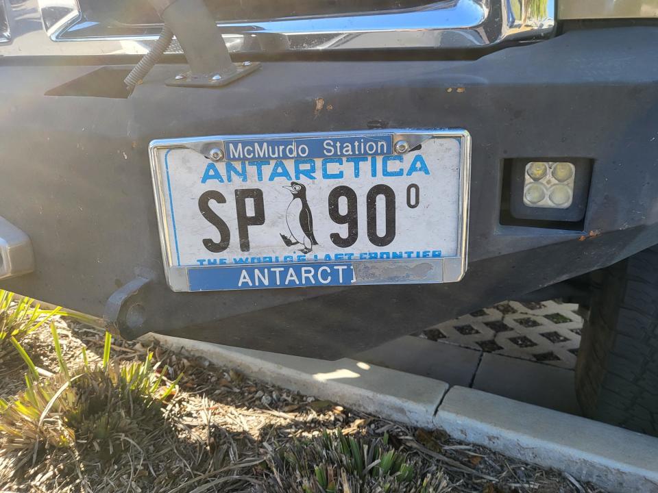 Antarctica license plate, with two letters and two numerals and a penguin in the middle of the plate and "The world's last frontier" slogan