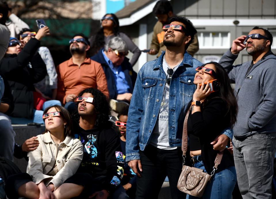 Clark University students Shreyas Sharma and Aarti Rathod, standing at right, and Dawn Friedman and Ganesh Paibodi, seated left, watch the partial solar eclipse at Worcester Town Common. 
(Credit: Allan Jung/Telegram & Gazette)