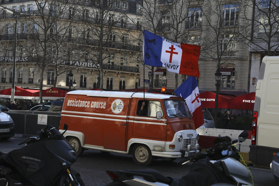 A demonstrator holding a French flag decorated with the Gaullist cross, drives up the Champs-Elysees avenue during a protest, Saturday, Feb.12, 2022 in Paris. Paris police intercepted at least 500 vehicles attempting to enter the French capital in defiance of a police order to take part in protests against virus restrictions inspired by the Canada's horn-honking "Freedom Convoy." . (AP Photo/Adrienne Surprenant)