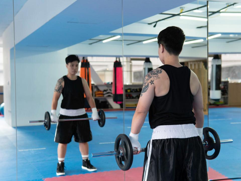 an athlete in shorts and a tank top looking into a mirror while lifting a small barbell