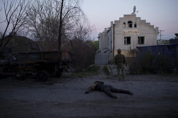 A Ukrainian serviceman stands next to the body of a suspected Russian soldier, in the village of Vilkhivka, recently retaken by Ukraininan forces near Kharkiv, Ukraine, Monday, May 9, 2022. (AP Photo/Felipe Dana)