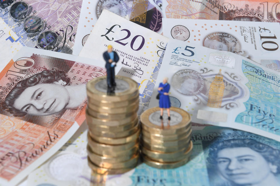 Models of a man and woman stand on a pile of coins and bank notes.