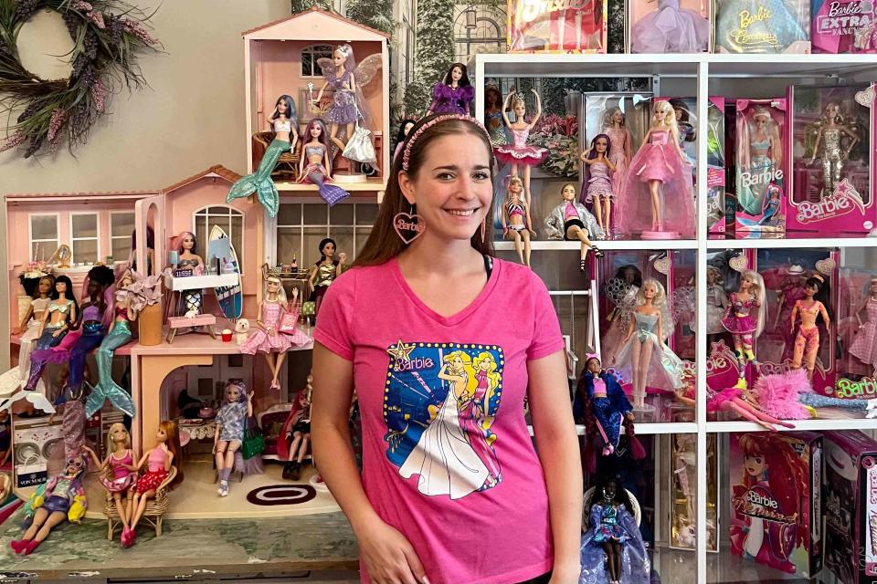 <p>Noah Volain</p> Ilana Volain standing in front of part of her collection of loose and boxed dolls in her home.