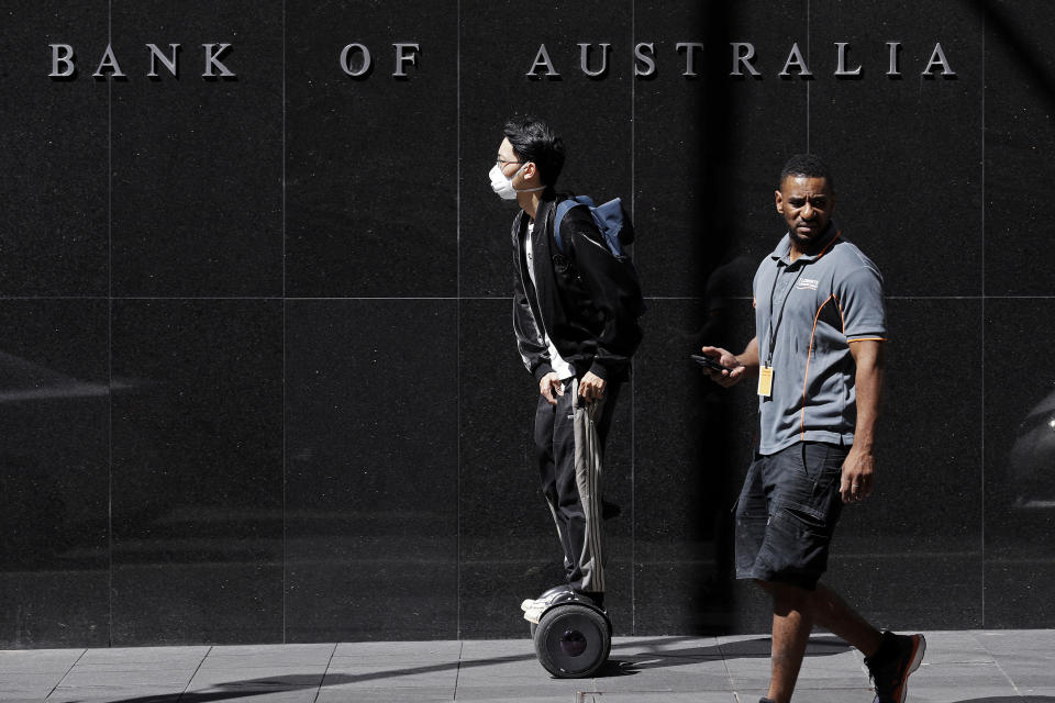 FILE - In this March 19, 2020, file photo, a man wearing a mask, left, rides a personal transporter past the Reserve Bank of Australia in Sydney. The coronavirus pandemic pushed Australia’s economy into recession for the first time in 29 years in the first quarter of the year 2022, and the situation is expected to get worse. (AP Photo/Rick Rycroft, File)