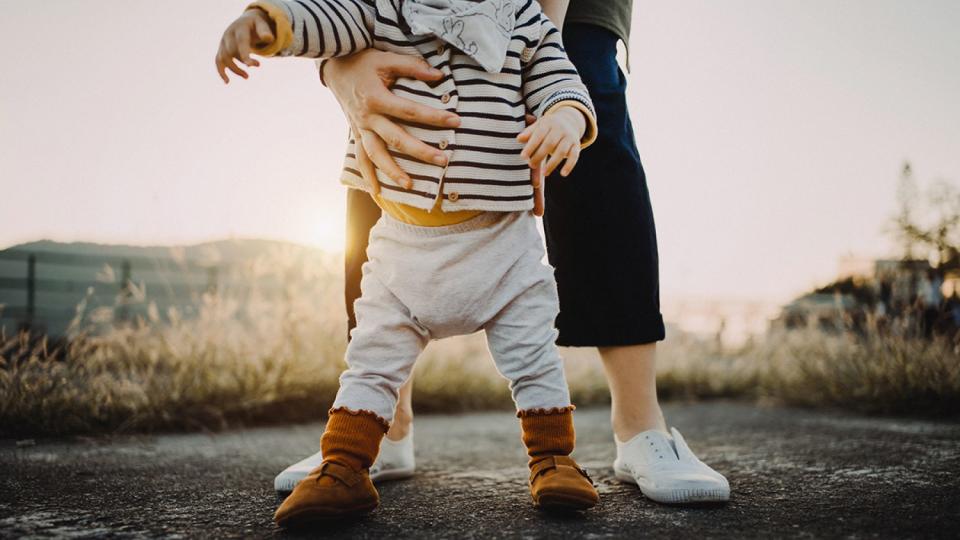 Mother holding baby daughter's body helping her to take her first step in life