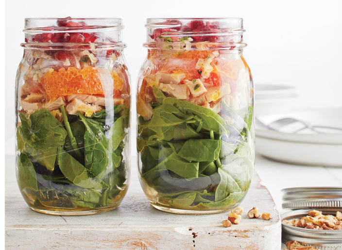 mason jar salad with spinach, turkey, cara cara oranges, and pomegranate seeds on wooden tray with jar of nuts and white plate