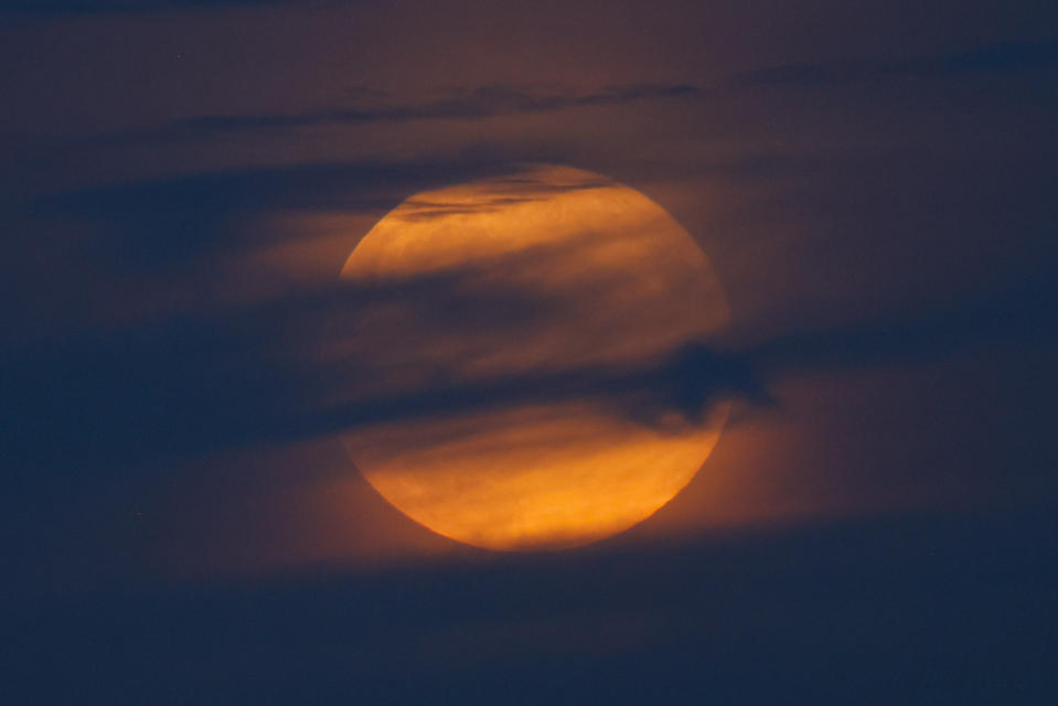 a fully, hazy moon hides behind wispy clouds