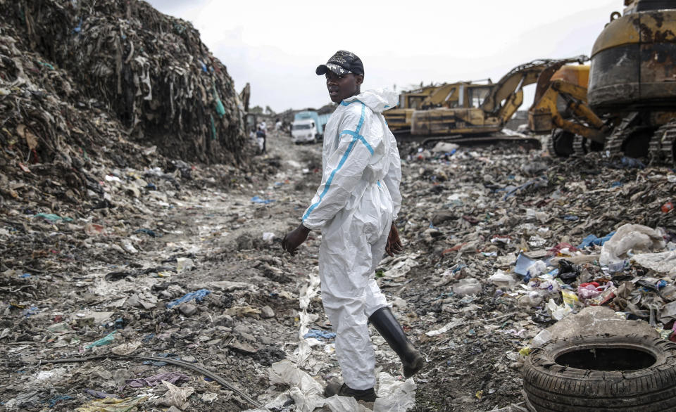 Isaac Kivai scavenges recyclable materials for a living at Dandora, the largest garbage dump in the Kenyan capital of Nairobi, Sunday, March 28, 2021. He wears a protective medical suit he and his friends had found in the trash. The waste pickers say the gear protects them from the weather during the rainy season. (AP Photo/Brian Inganga)