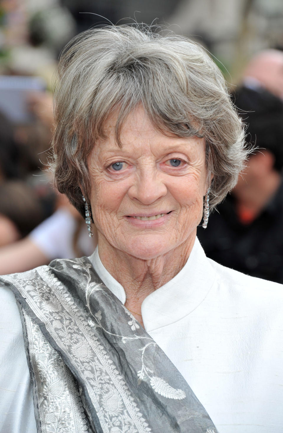 Maggie Smith smiling at a public event, wearing a white outfit with an elegant silver and white shawl