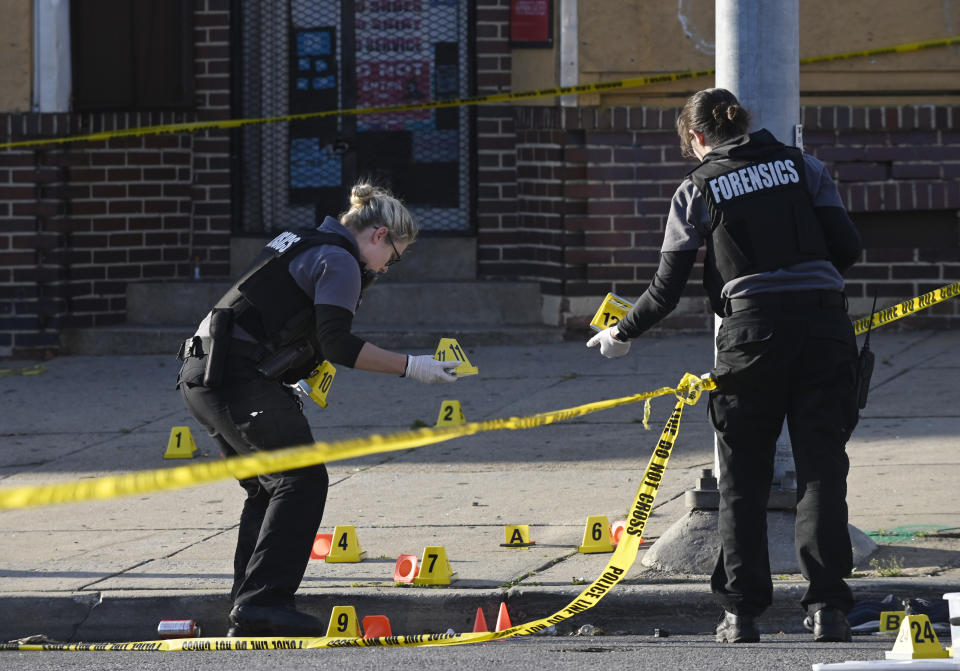 Baltimore police forensics officers place evidence markers next to bullet casings while investigating the scene of a shooting in Baltimore on Sunday, April 28, 2019. A gunman fired indiscriminately into a crowd that had gathered for Sunday afternoon cookouts along a west Baltimore street, killing one person and wounding seven others, authorities said. (Kenneth K. Lam/The Baltimore Sun via AP)