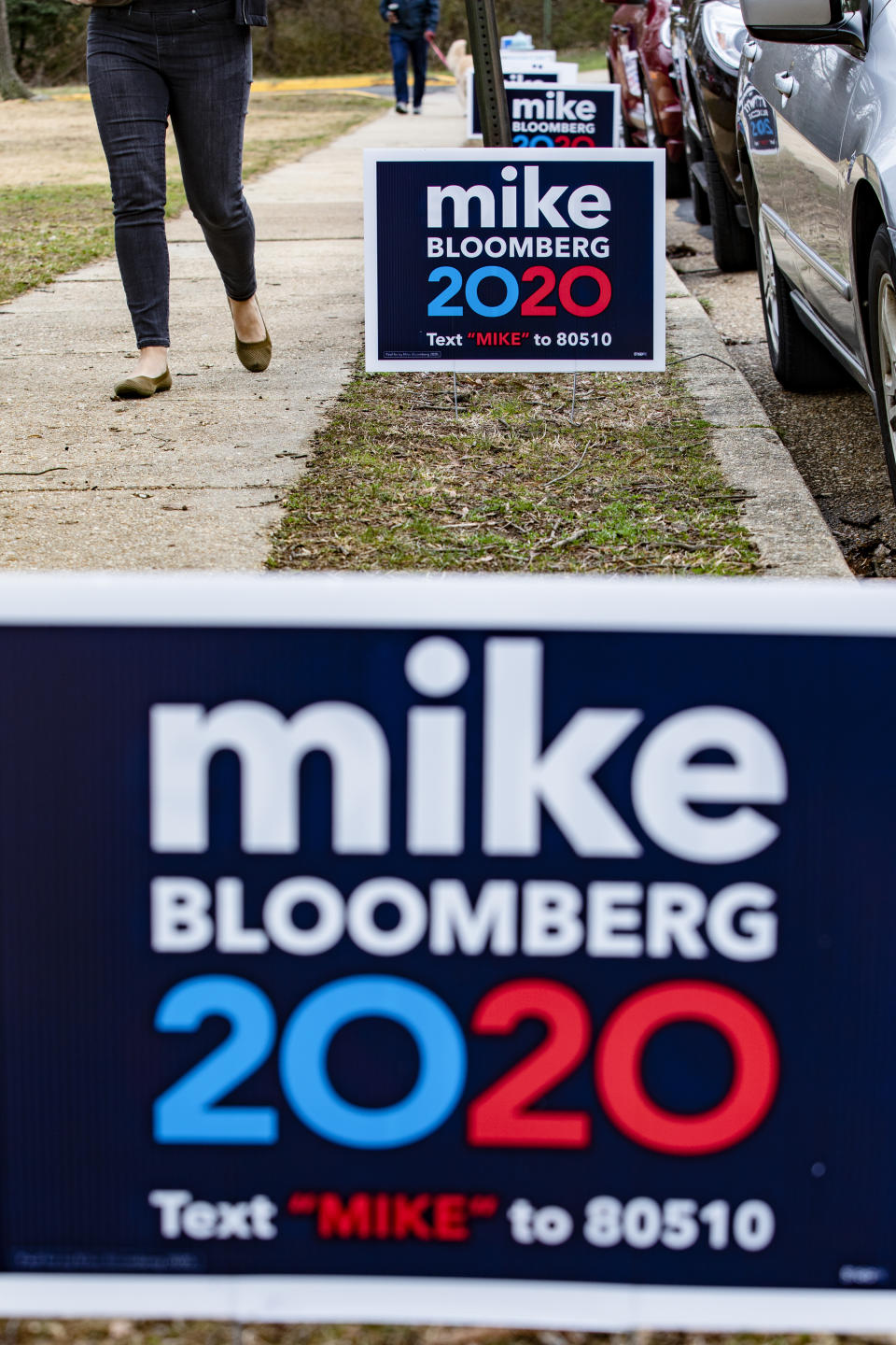 Person walking past Mike Bloomberg 2020 campaign signs on a sidewalk