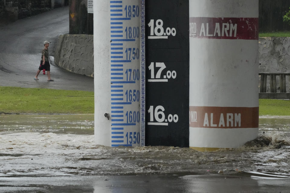 A man walks near a flood alert marker along a swollen river due to enhanced rains brought about by Typhoon Doksuri on Thursday, July 27, 2023, in Marikina city, Philippines. Typhoon Doksuri lashed northern Philippine provinces with ferocious wind and rain Wednesday, leaving several people dead and displacing thousands of others as it blew roofs off houses, flooded low-lying villages and triggered dozens of landslides, officials said. (AP Photo/Aaron Favila)